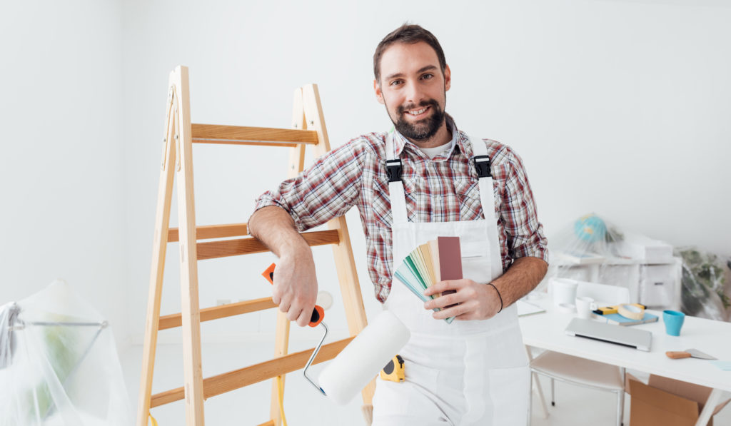 Confident professional painter posing, he is holding a paint roller and color swatches, home renovation and decoration concept